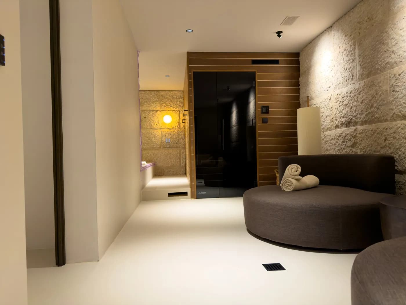 Übergang vom Gang zur Sauna: Naturstein, Holz und die fugenlose Bodenfläche verbinden sich zu einem stimmigen Spa-Bereich.